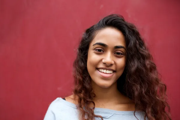 Therapy for individuals: a smiling young woman with long curly hair against a red wall